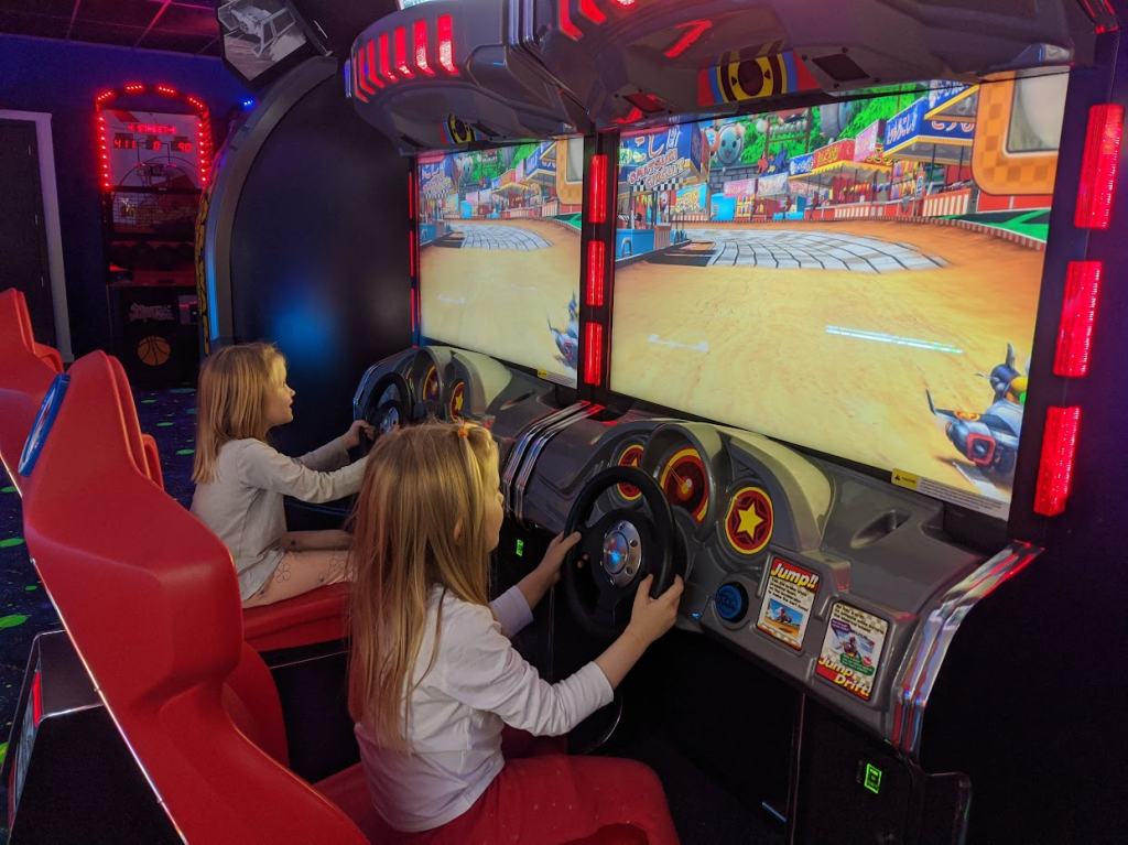 Two children play an arcade version of Mario Kart.